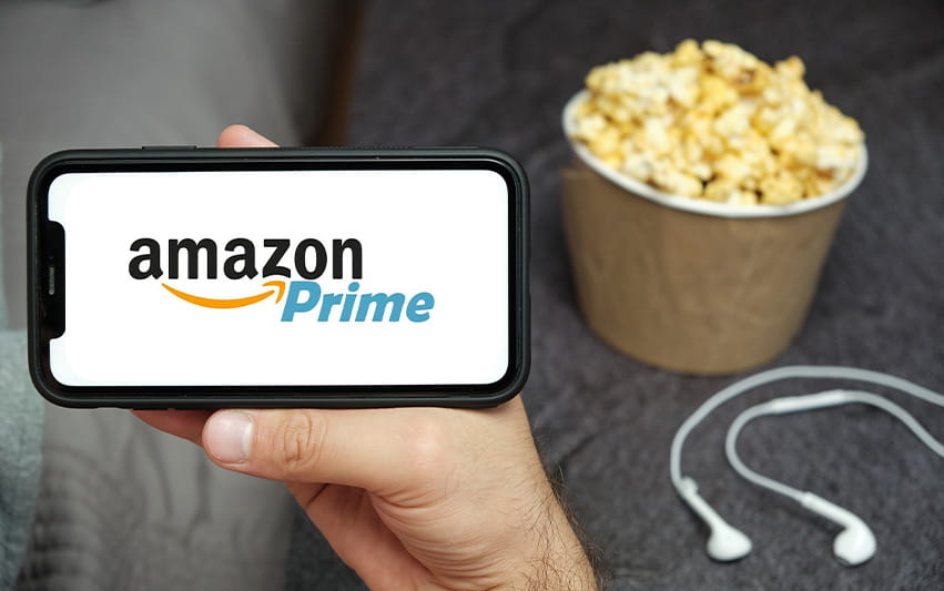 Auf einem Handy ist Amazon Prime Video zu sehen sowie eine Schüssel Popcorn im Hintergrund davon 