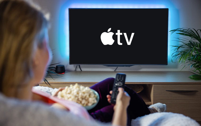 Frau ist von hinten auf der Couch zu sehen, hat Popcorn neben sich und schaut Apple TV