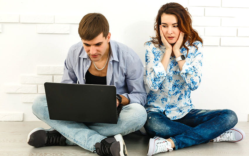 Zwei Menschen sitzen vor einem Laptop und schauen auf diesen